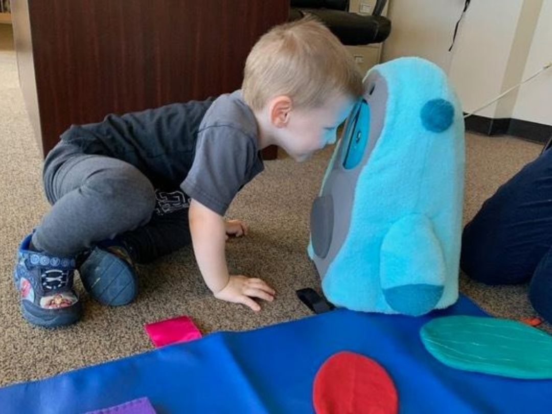 young boy playing with blue robot on ground